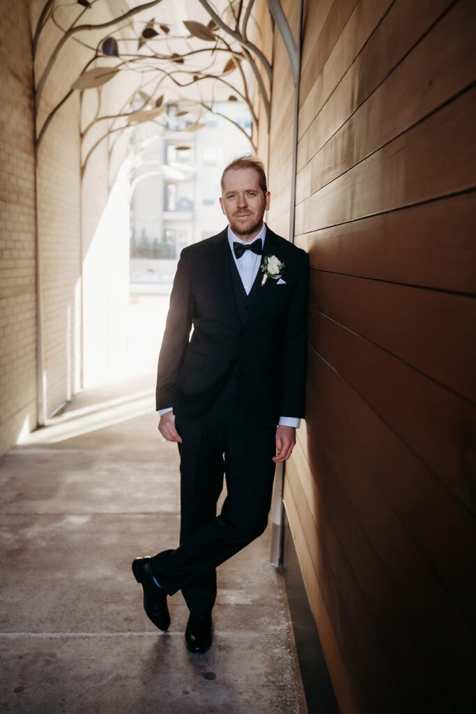 Groom leans against a wall in a stylish downtown Denver alleyway, looking relaxed and confident post-ceremony.