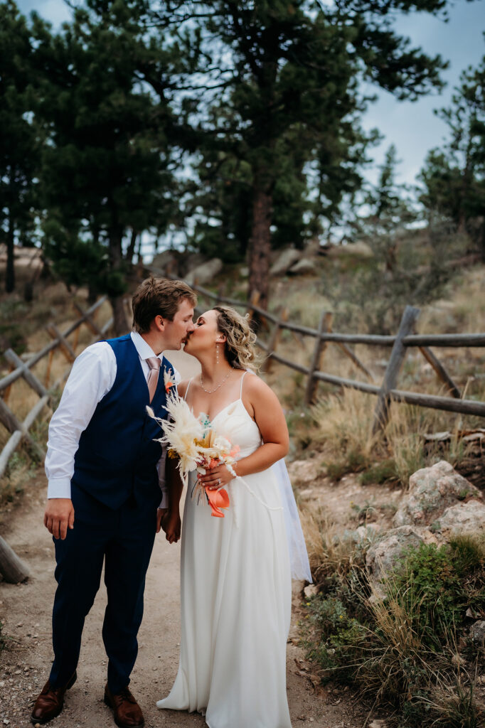 Couple shares a kiss on a rustic trail lined with wooden fencing after their ceremony.