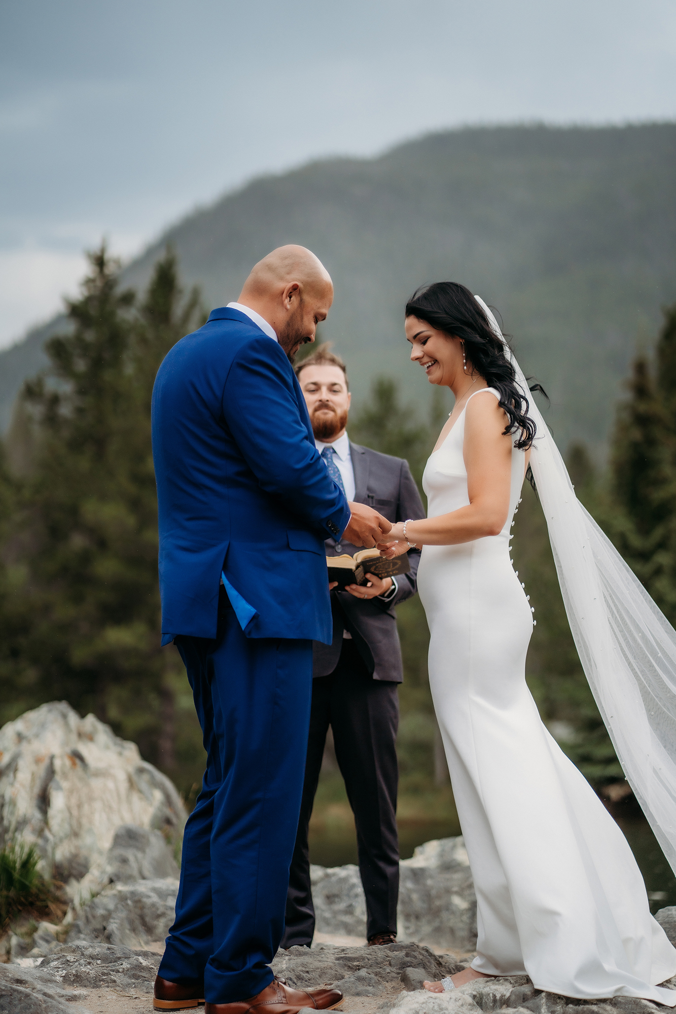 Bride places a ring on the groom’s finger during their outdoor vow exchange, smiles full of emotion.