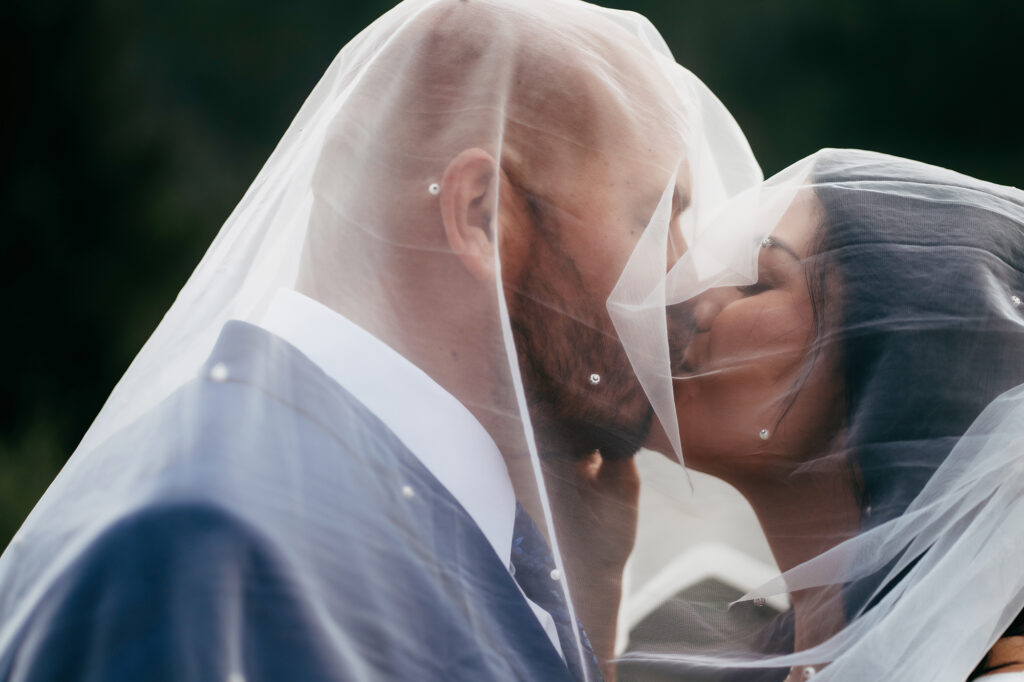 Close-up of a romantic veil kiss between a bride and groom, soft tulle framing their faces.