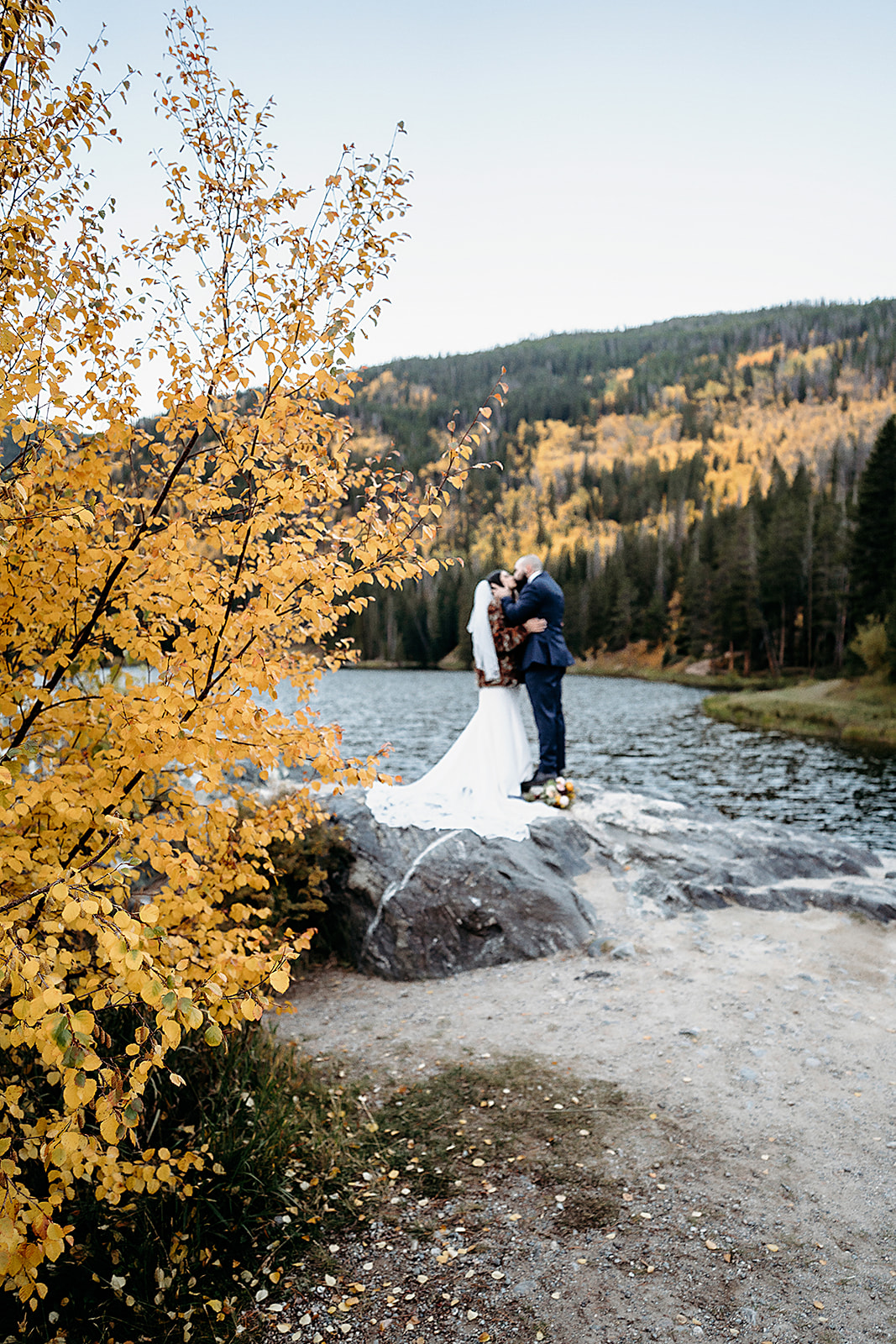 The bride and groom share a kiss during their adventure elopement, surrounded by vibrant yellow aspens and the shimmering waters of an alpine lake.
