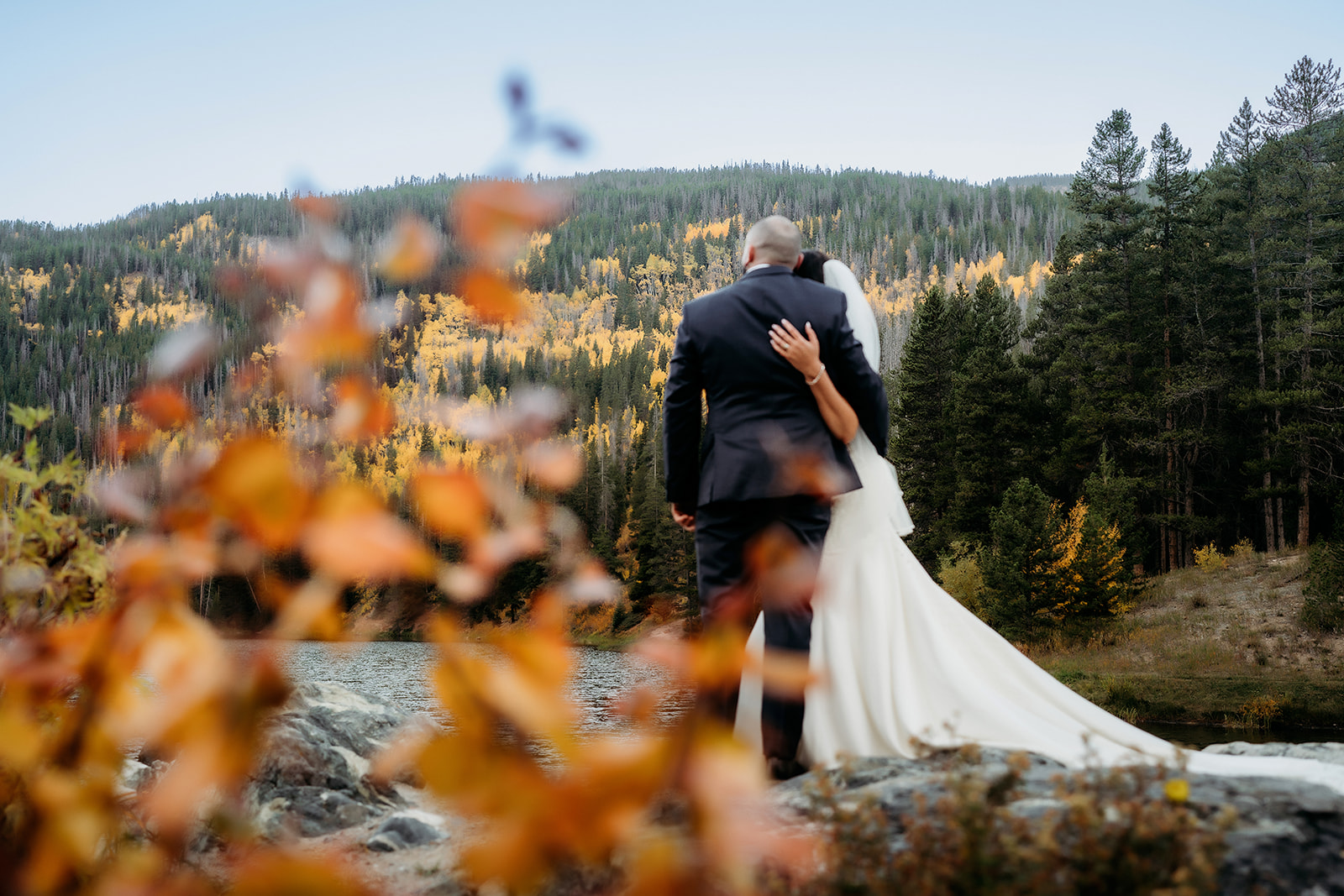 A bride and groom hold each other close, gazing out over a vibrant Colorado landscape of golden aspens and evergreens during their adventure elopement.
