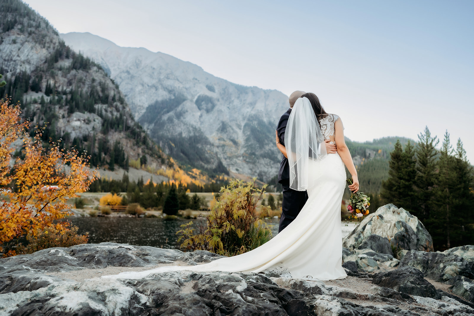 The couple stands together on a mountain overlook, taking in the sweeping views of Colorado’s dramatic peaks and vibrant fall colors.
