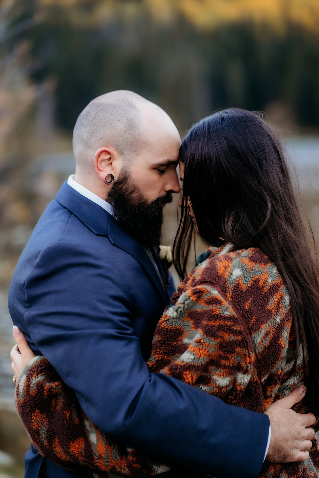 The couple shares a quiet, emotional moment with their foreheads pressed together, wrapped in love and a cozy fall jacket beneath mountain light.