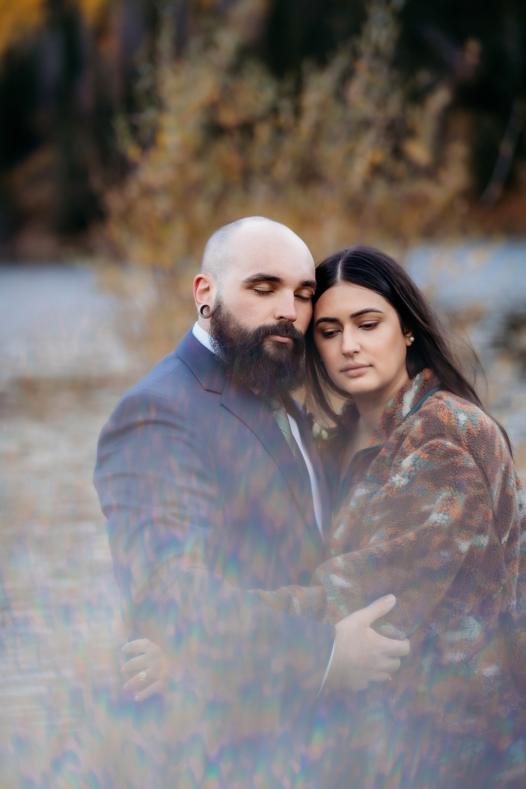 A peaceful portrait of an eloping couple holding each other close with soft light and dreamy bokeh surrounding them in a quiet forest clearing.