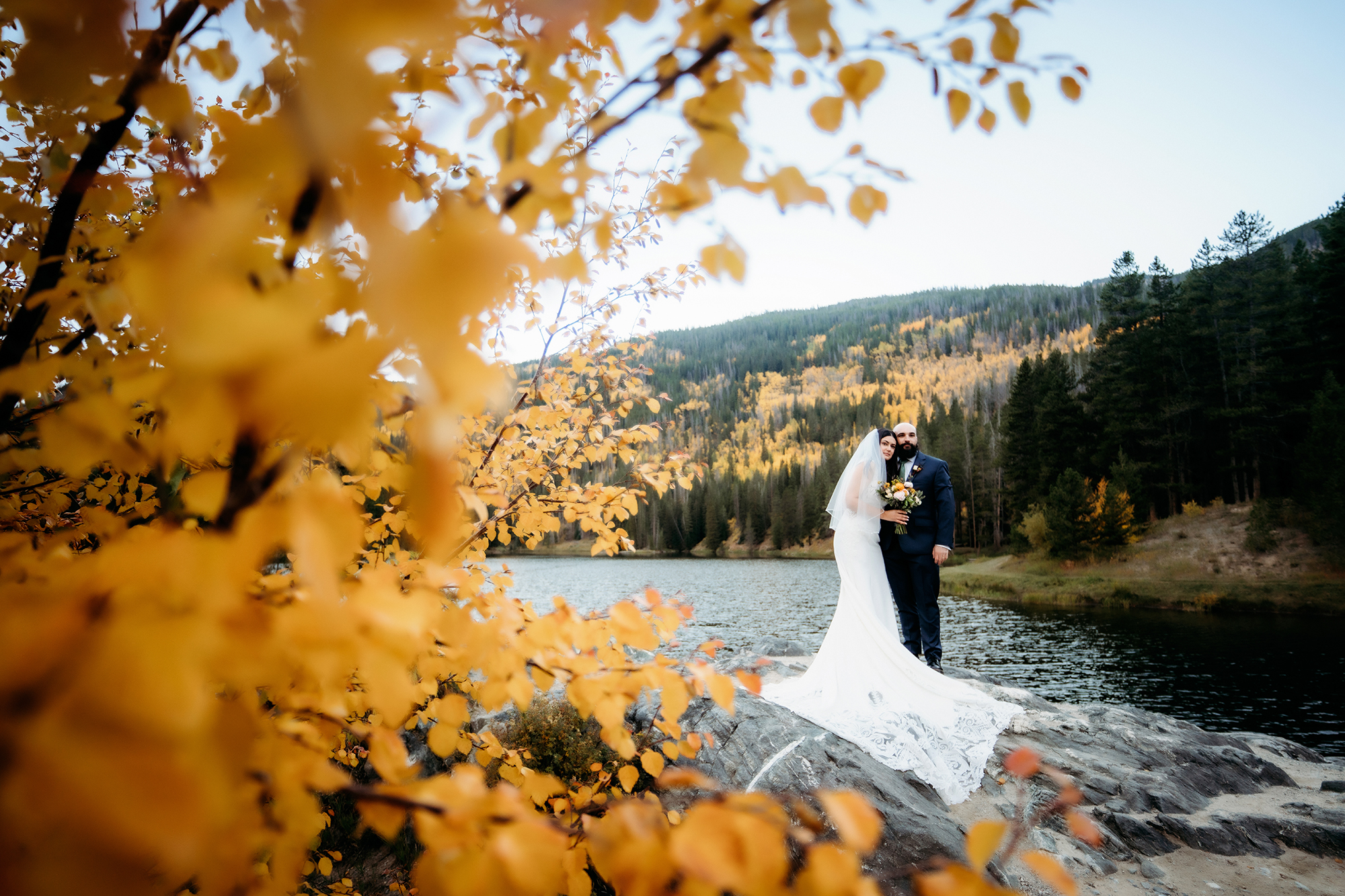 Framed by vibrant golden foliage, the couple shares a sweet kiss on a rock by the lake—an iconic Colorado adventure elopement portrait full of color and romance.