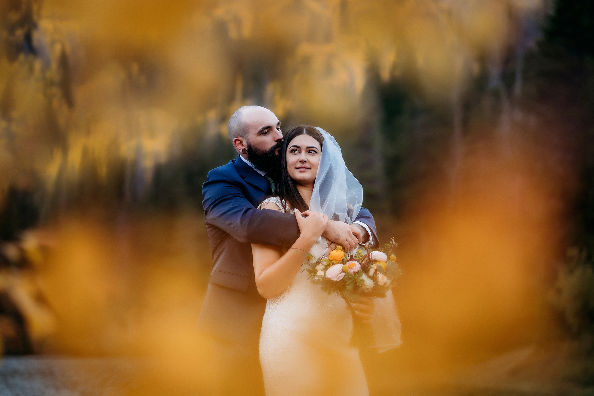 The groom cradles his bride from behind as they stand in a golden aspen grove, wrapped in the peaceful quiet of their fall adventure elopement.