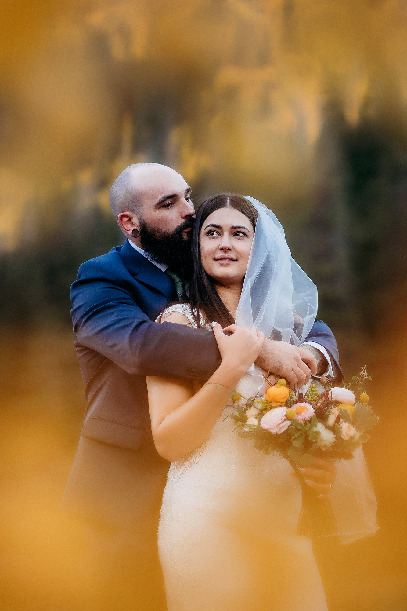 Framed by soft golden foliage, the groom wraps his arms around the bride as she holds her bouquet, the two sharing a quiet embrace during their fall adventure elopement in the Colorado mountains.