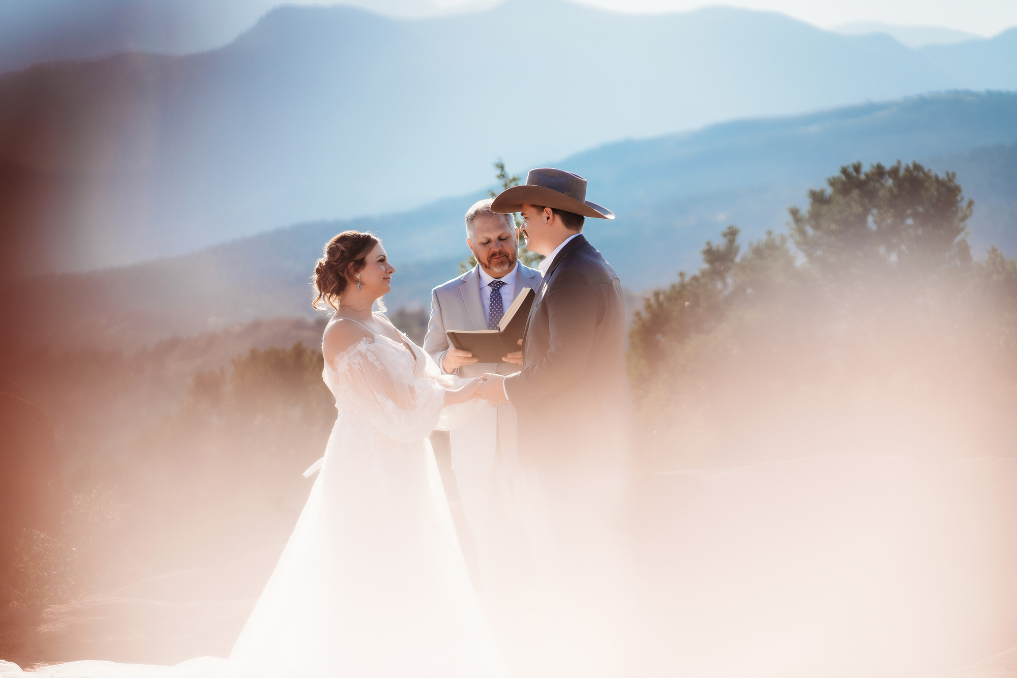 Bride and groom walking hand in hand through natural terrain with red rocks and greenery during Denver elopement.