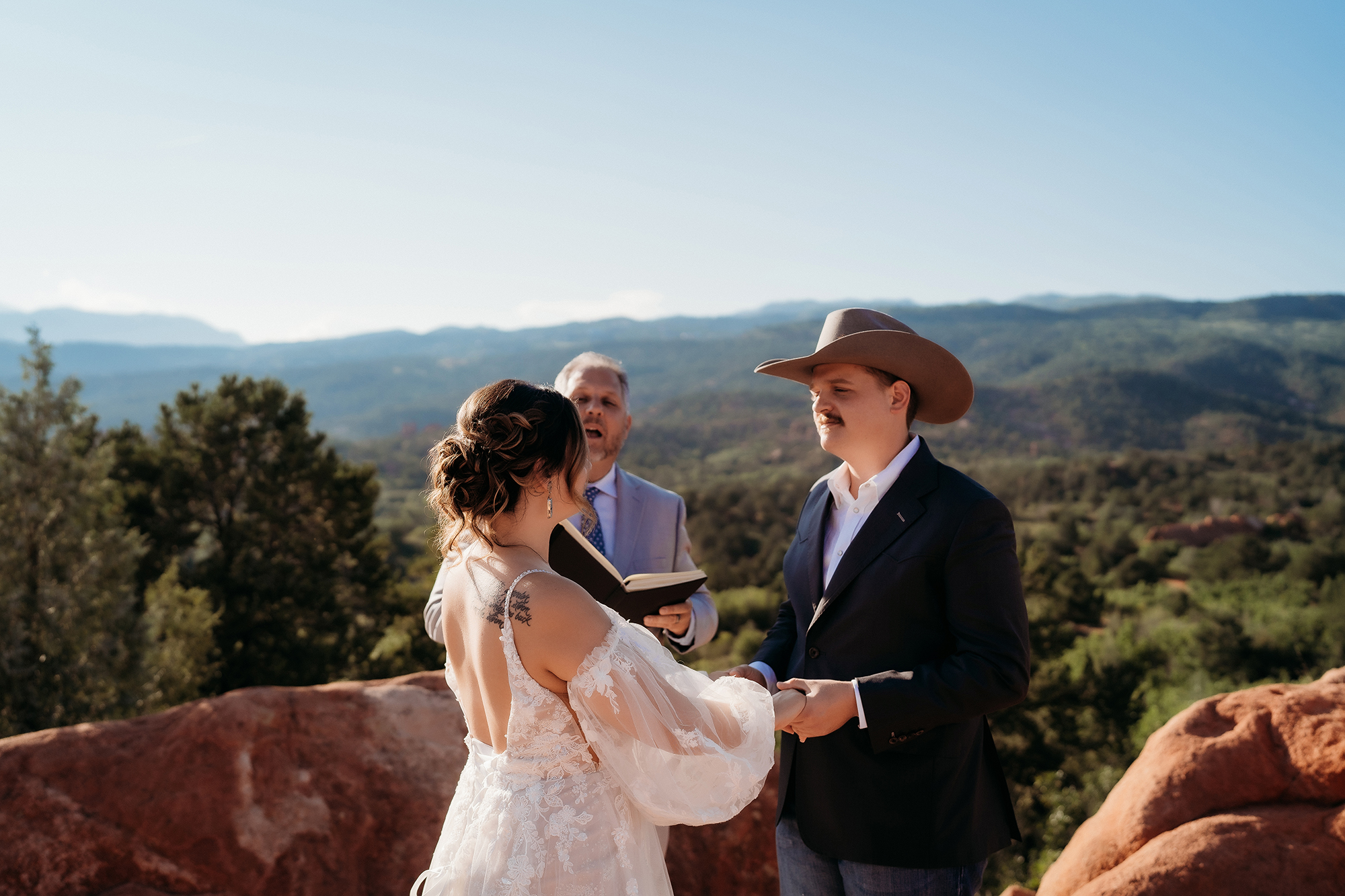 Bride and groom holding hands during their intimate Denver elopement ceremony surrounded by rocky terrain and lush greenery.