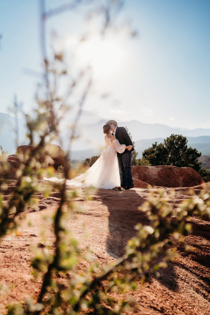Bride and groom sharing a kiss on a sunlit red rock outcrop during their Denver elopement.