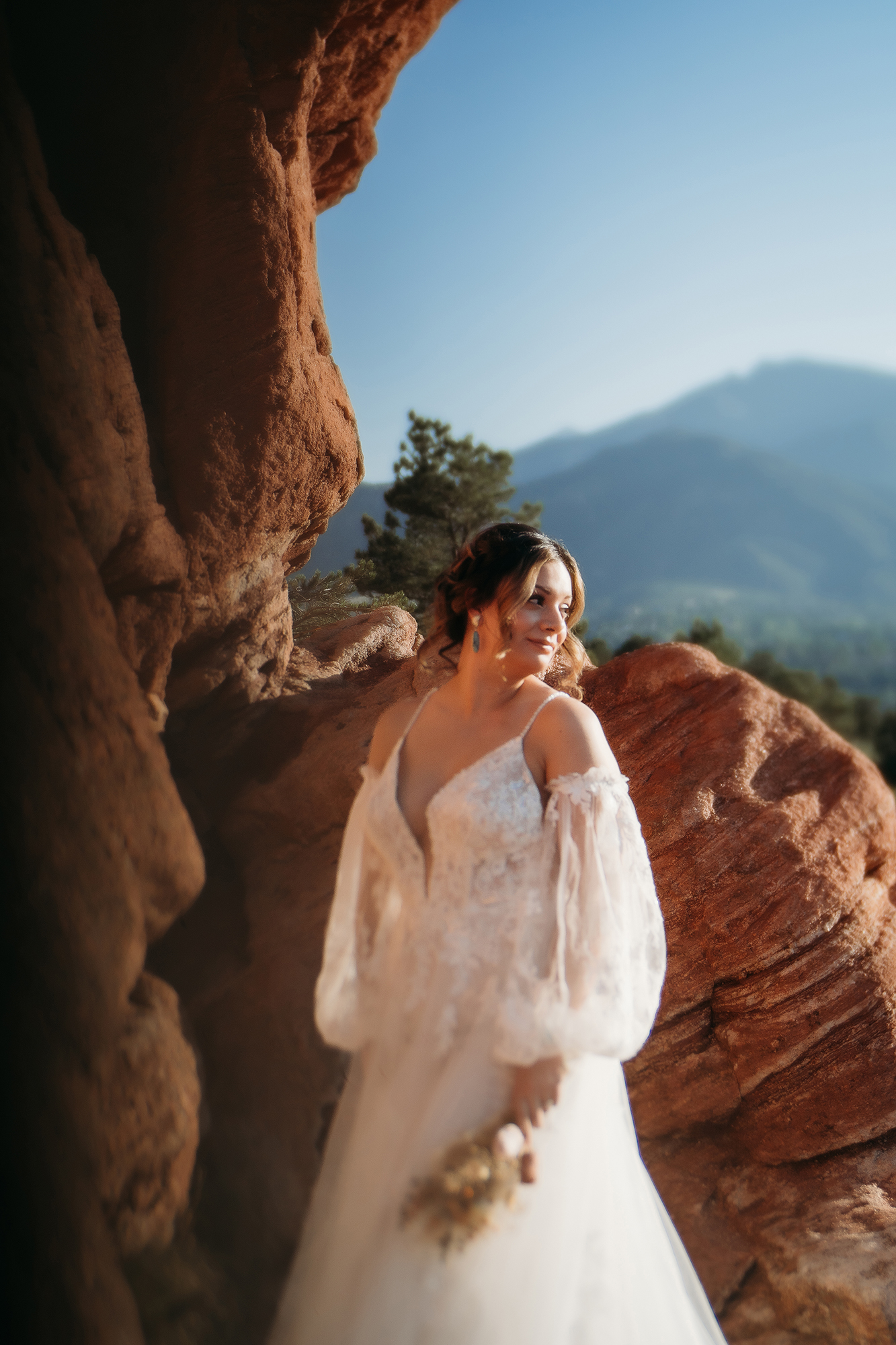 Bride standing with bouquet near red rock formations bathed in warm sunlight during a Denver elopement.