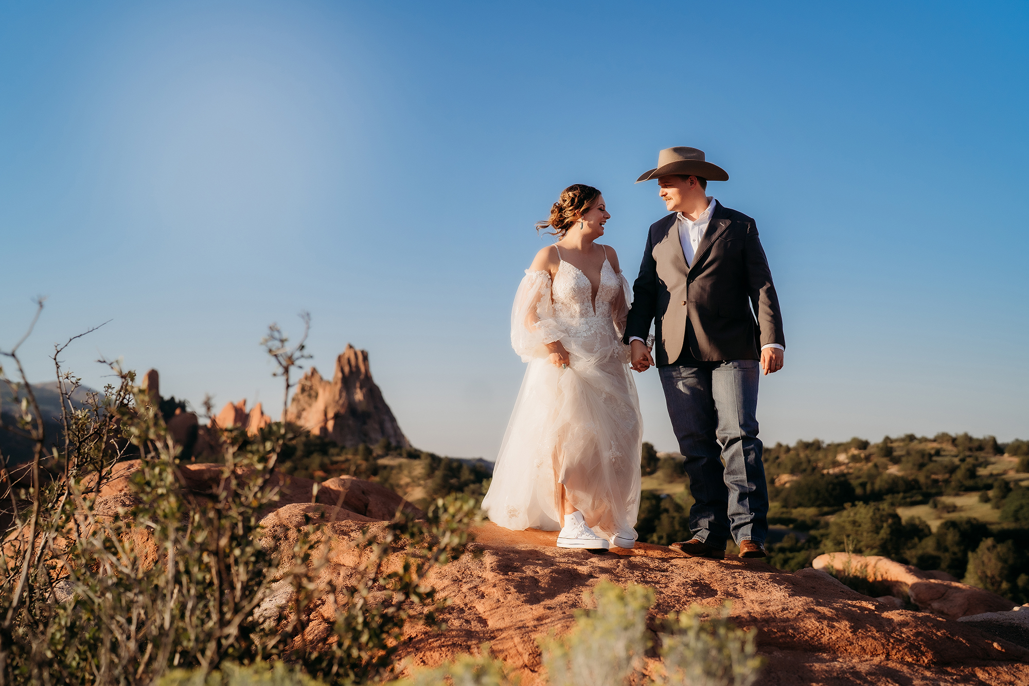 Bride and groom walking together with warm golden sunlight illuminating their wedding attire on red rock formations at Denver elopement.