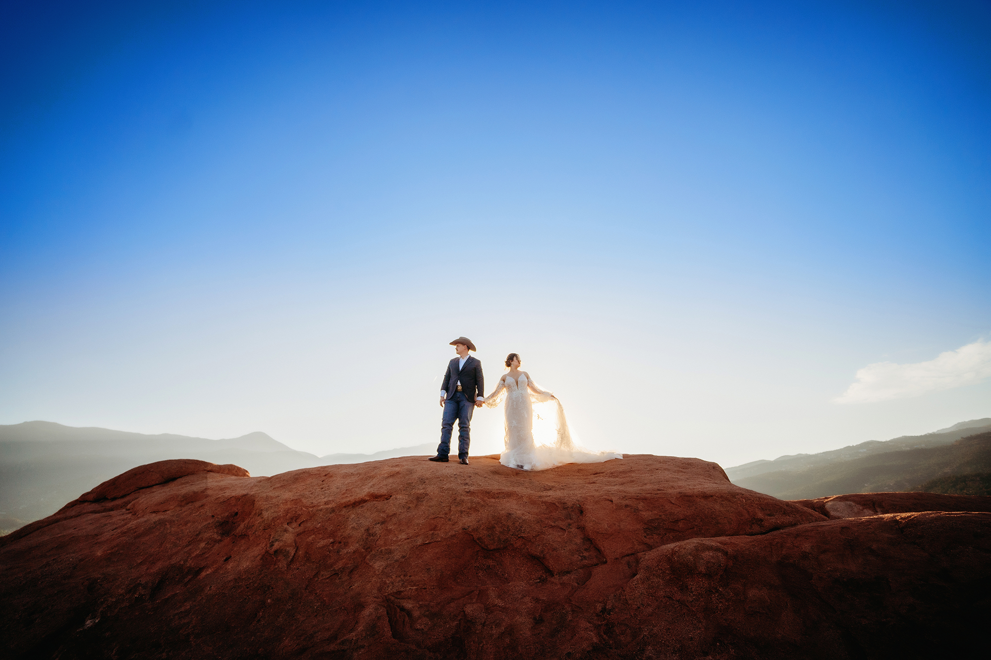 Couple standing hand in hand on a red rock overlook with sun setting behind them during a Denver elopement.