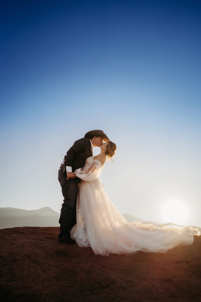 Bride and groom holding hands and gazing into each other’s eyes on a red rock formation at sunset in Denver.