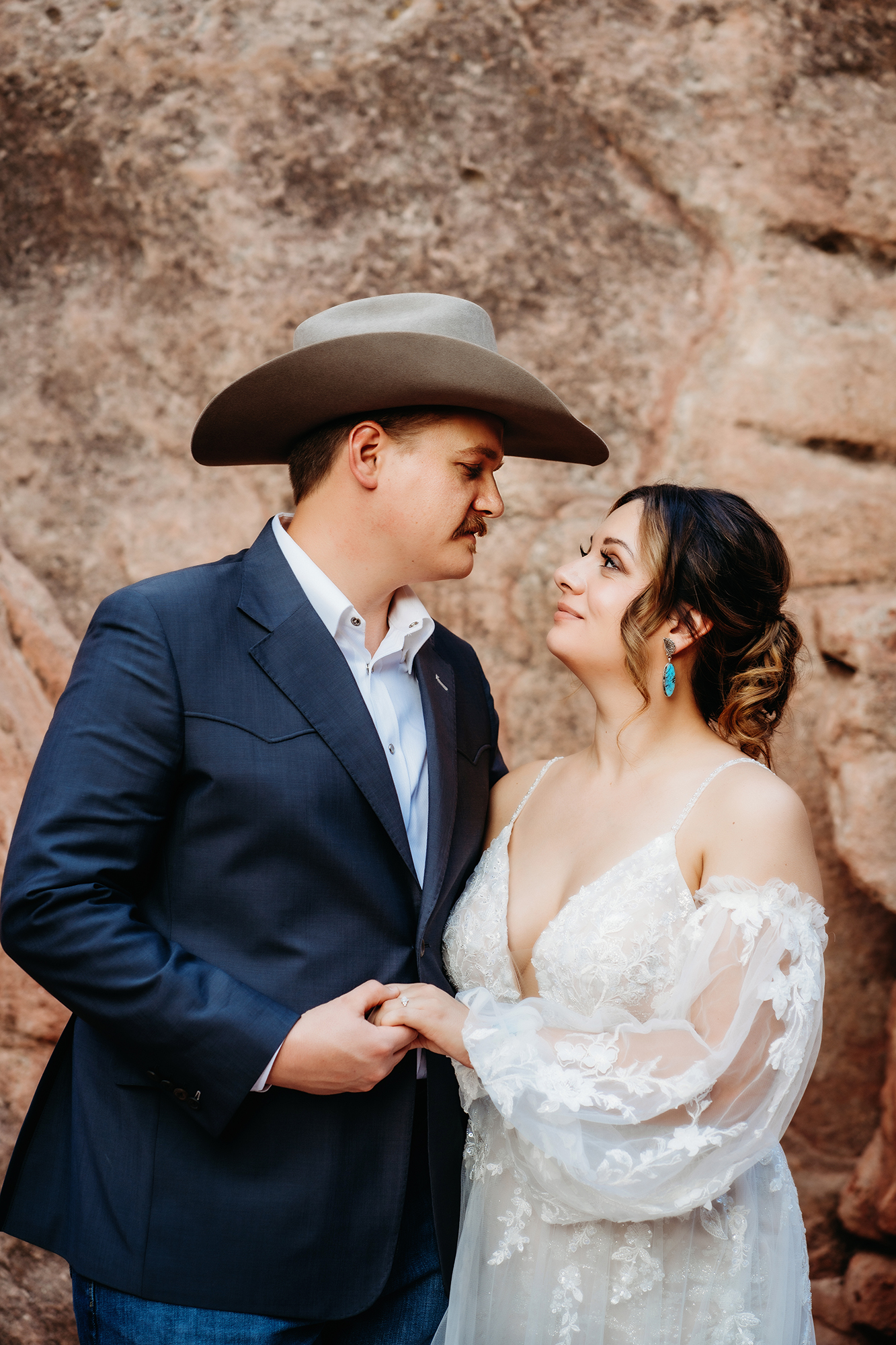 Bride and groom holding hands and gazing into each other’s eyes near red rocks during their Denver elopement session.