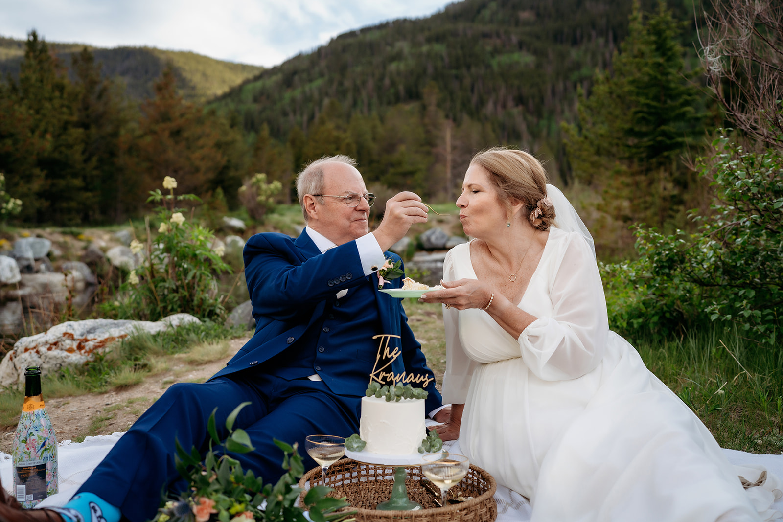 The couple shares cake on a mountaintop picnic, showing How to Make Your Elopement Special with a scenic and intimate celebration.