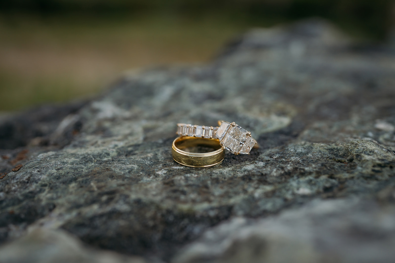 A gold wedding band and diamond ring sit atop a textured rock, symbolizing love grounded in nature.