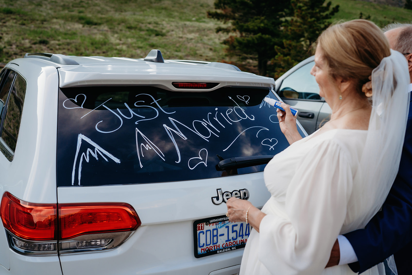 The bride adds the finishing touch to a “Just Married” message on their getaway car—a playful and memorable moment.