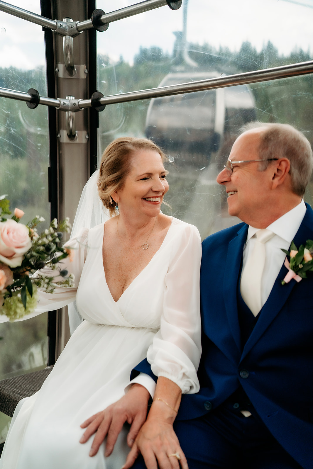 The couple shares a sweet moment inside a gondola cabin, surrounded by mountain views and floral details—adding adventure to their special day.