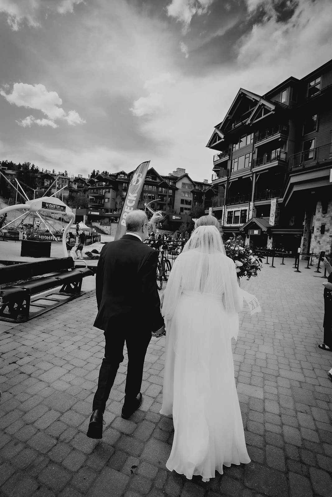 The couple walks hand-in-hand through a rustic village plaza, captured in timeless black and white for an added sense of nostalgia.
