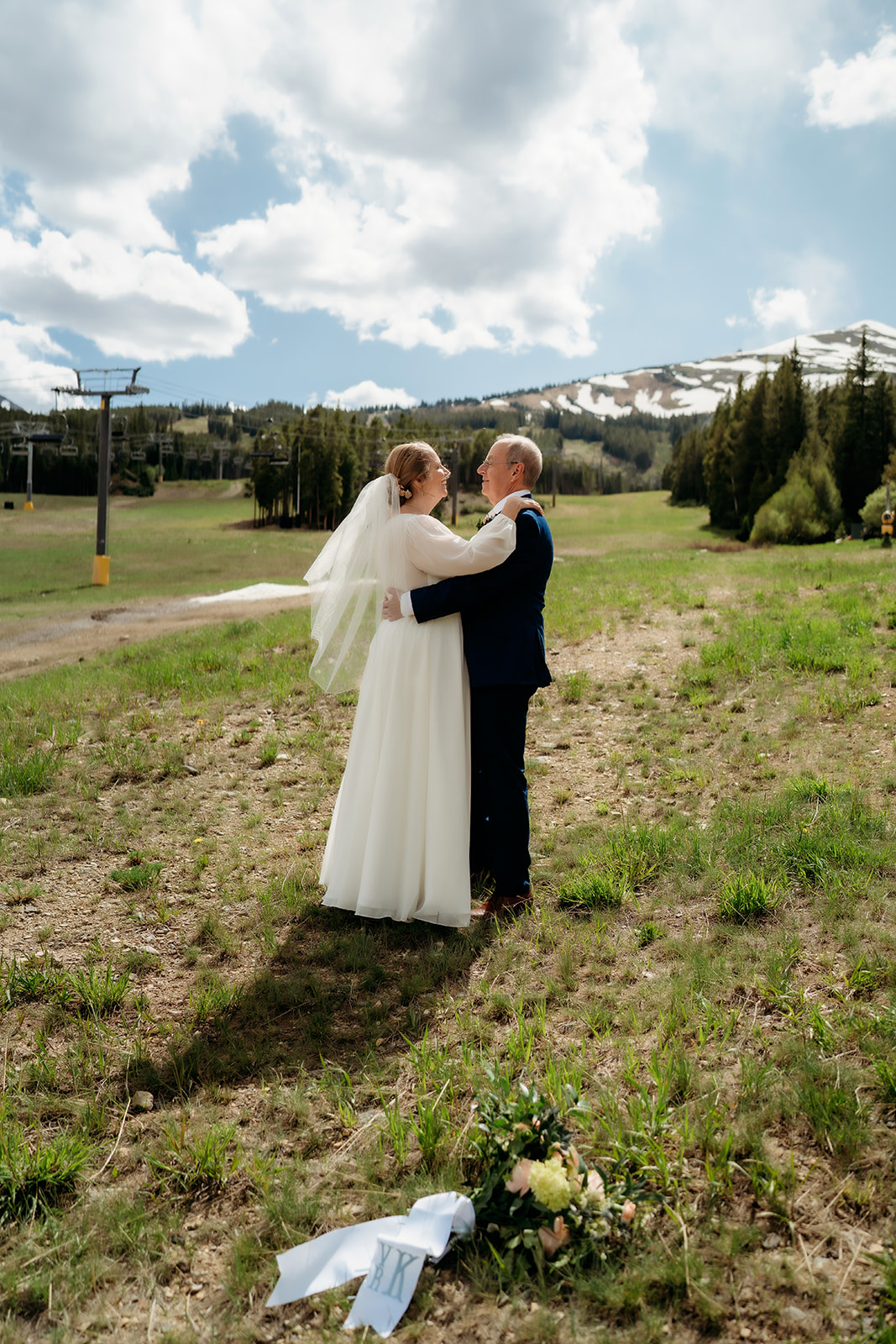 A bride and groom share a private dance in an alpine meadow beneath blue skies and snowy peaks—showcasing How to Make Your Elopement Special with unforgettable scenery.