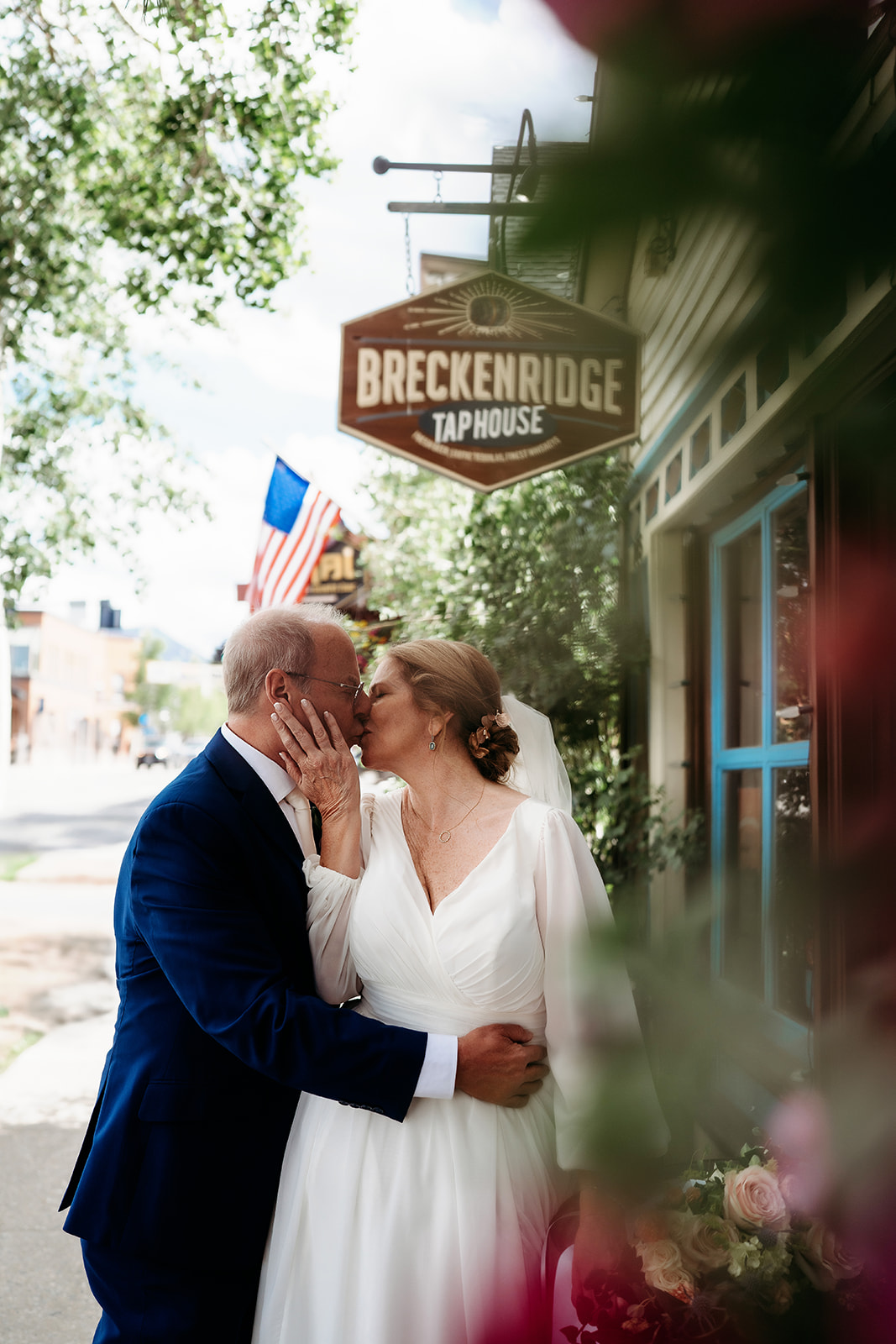 Bride and groom share a romantic kiss outside the Breckenridge Tap House, framed by soft flowers and small-town charm.