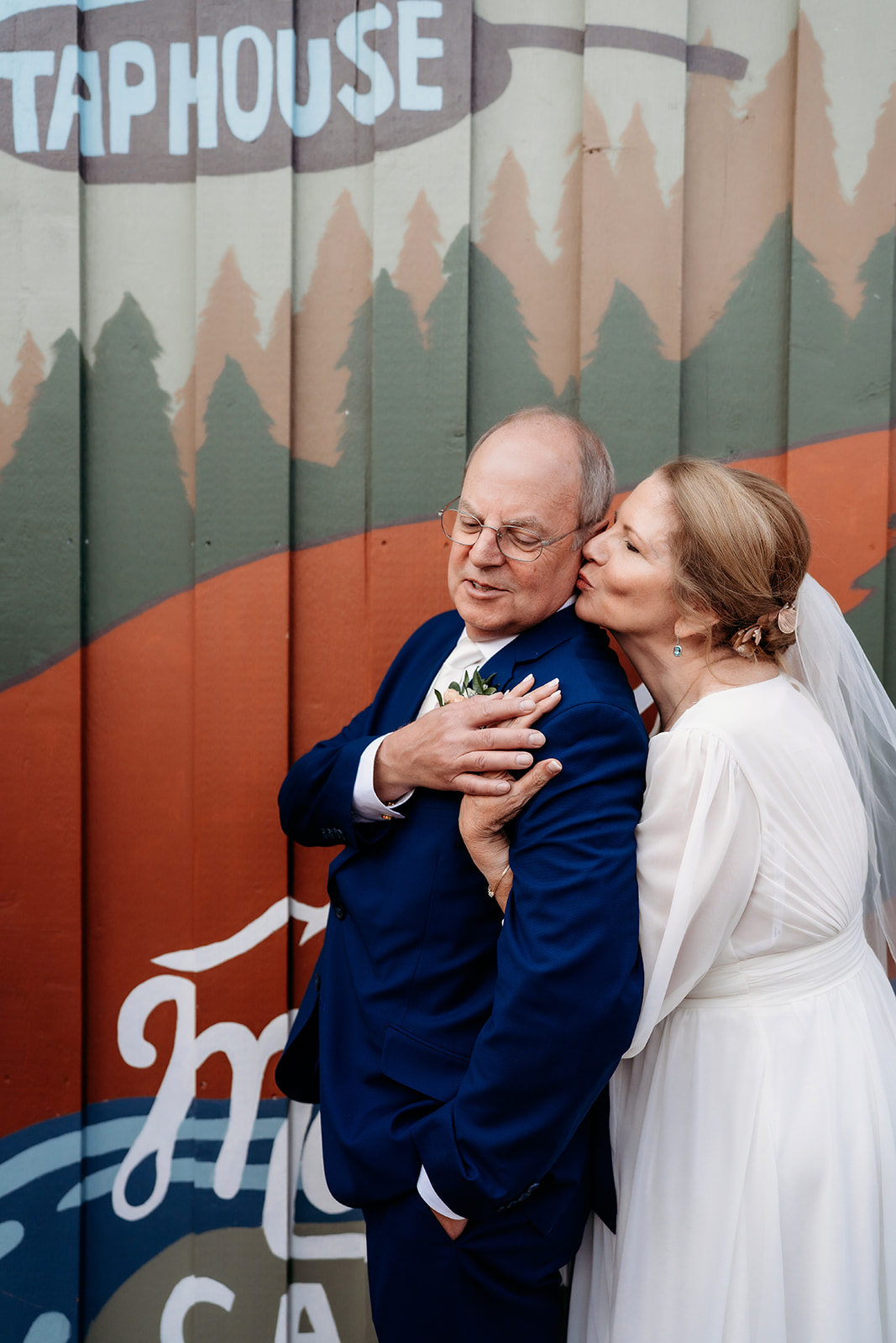 In a playful, urban twist, the bride kisses her groom beside a colorful mural—proof that How to Make Your Elopement Special can include personality and fun.
