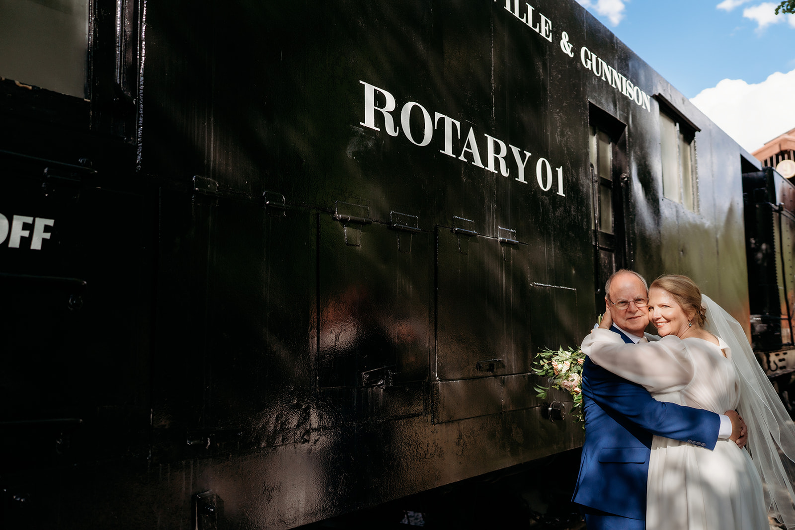 A sweet embrace as the couple stands beside the black Denver Leadville & Gunnison railway car—highlighting How to Make Your Elopement Special through unique backdrops.