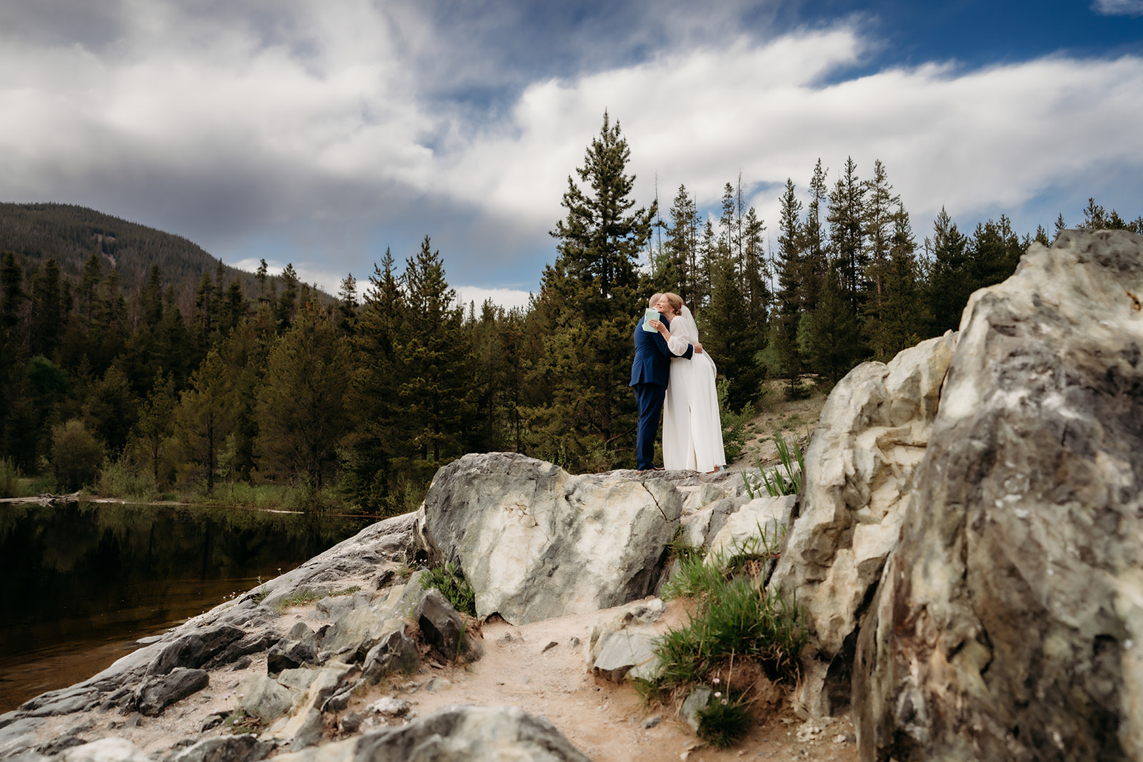 A quiet post-ceremony embrace between the couple, captured from a distance among towering trees and rocky terrain—showcasing How to Make Your Elopement Special through intimate moments.