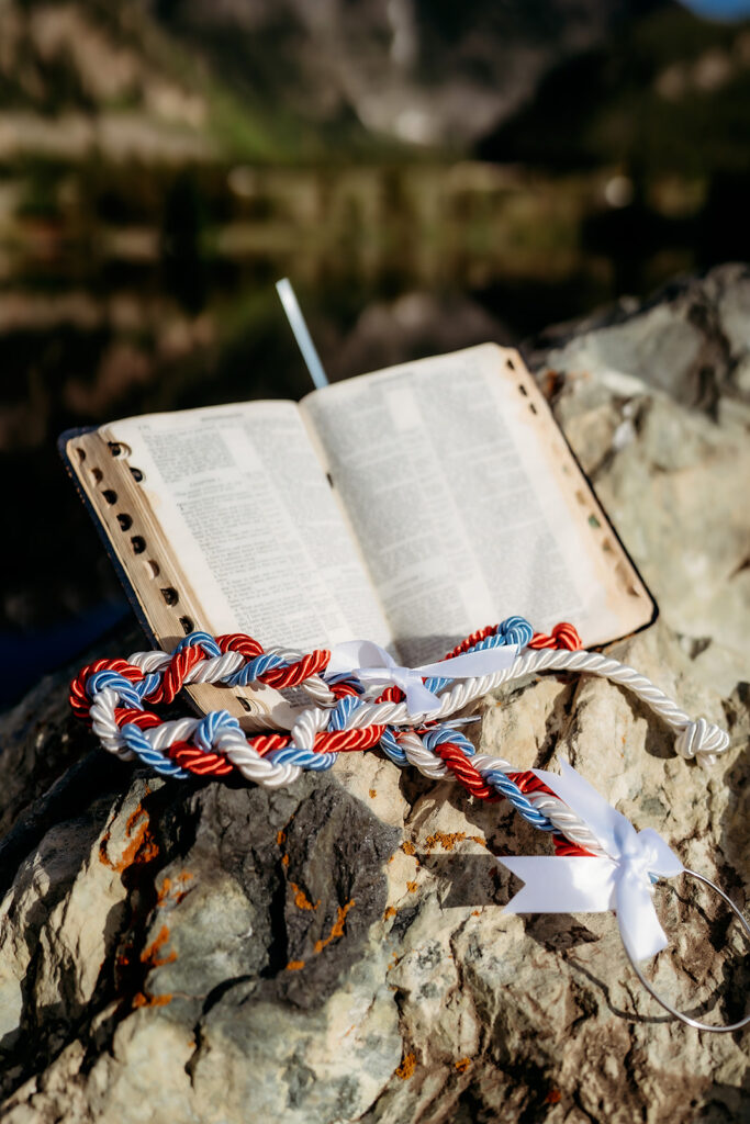 A red, white, and blue cord rests on an open Bible during a mountaintop ceremony, symbolizing unity and faith—adding a personal touch to How to Make Your Elopement Special.
