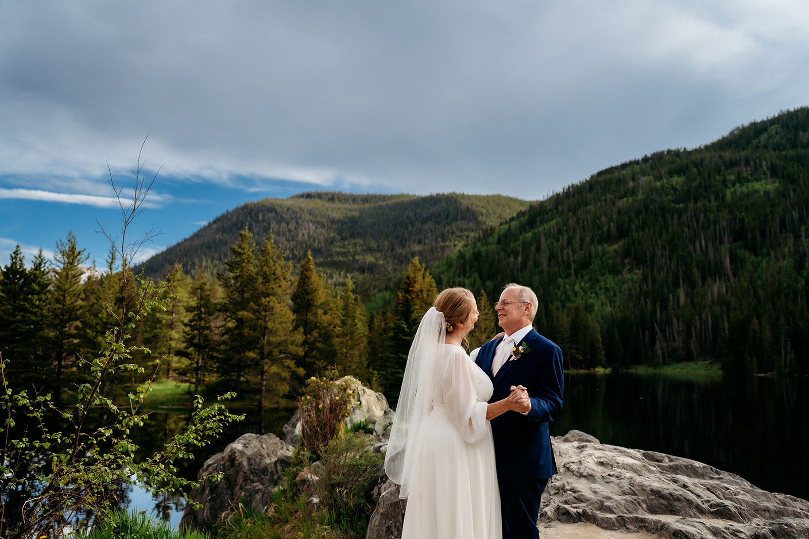 The bride and groom twirl in front of a reflective alpine lake—an unforgettable scene that shows How to Make Your Elopement Special.