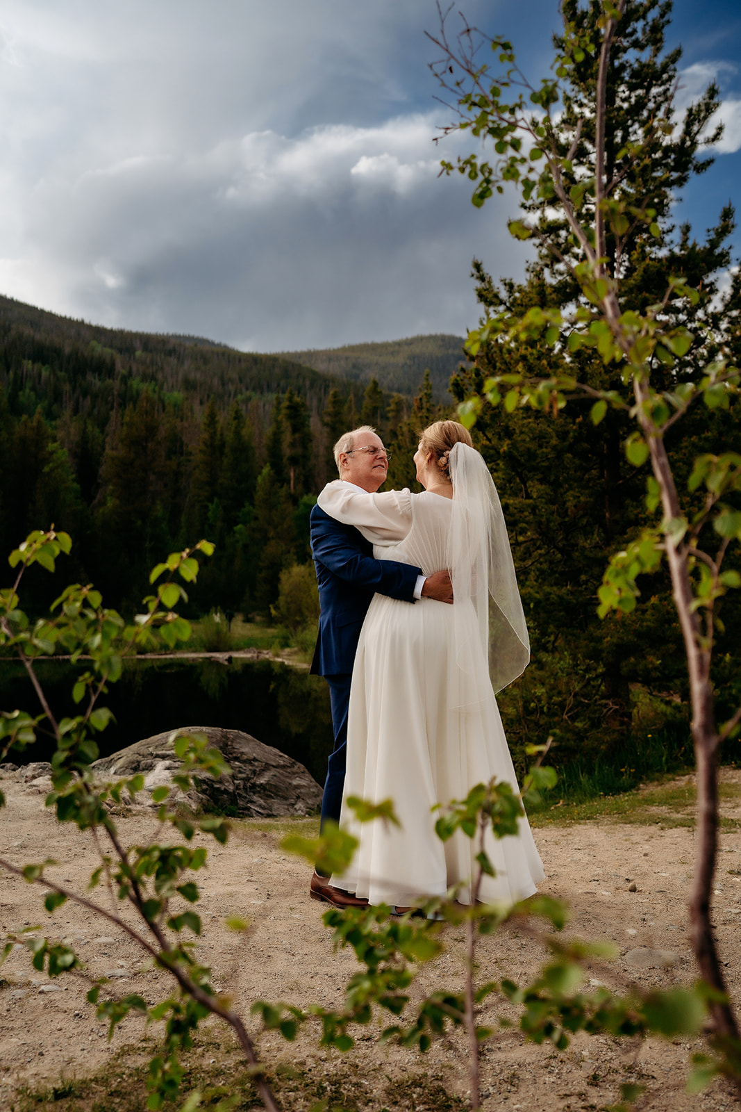Framed by mountain trees and a striking sky, the couple shares a slow dance outdoors—one of many ways to elevate your elopement experience.