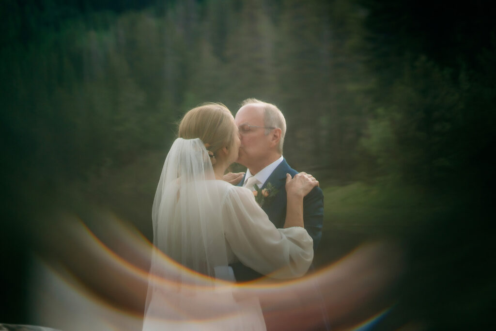 A magical moment as the couple kisses in the forest, highlighted by a dreamy rainbow lens flare—adding an artistic touch to How to Make Your Elopement Special.