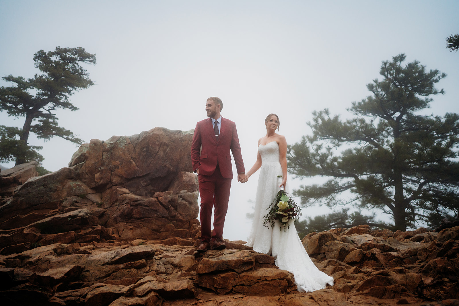 Couple holding hands on a rocky ridge with fog rolling in, demonstrating how to plan an elopement in the mountains.