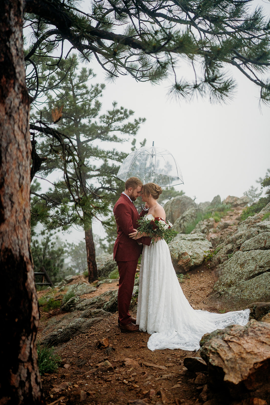 Bride and groom embrace on a misty mountain trail surrounded by trees, an intimate elopement moment.