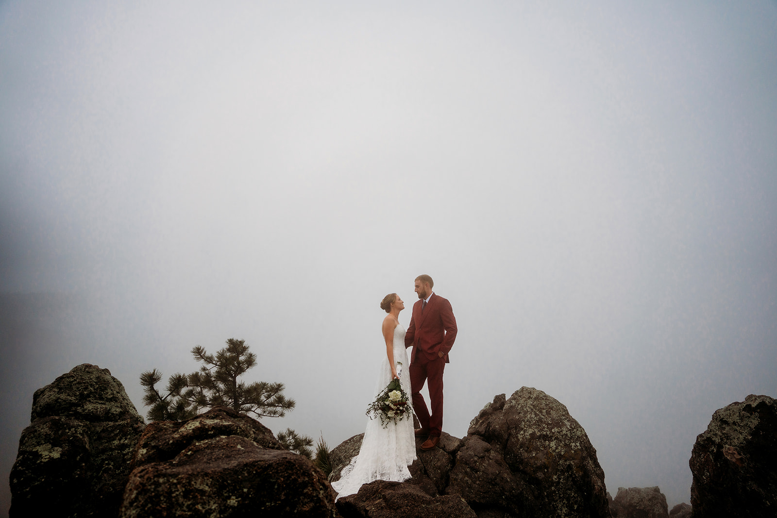 Couple stands together on a foggy mountain summit, an adventurous highlight of How to Plan an Elopement in the Rockies.