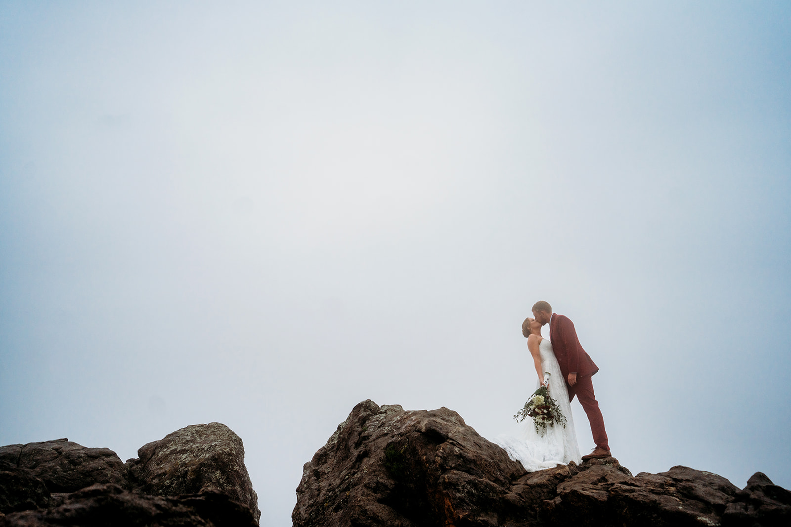 Couple kissing at the top of a mountain, framed by dramatic skies, an epic example of how to plan an elopement.