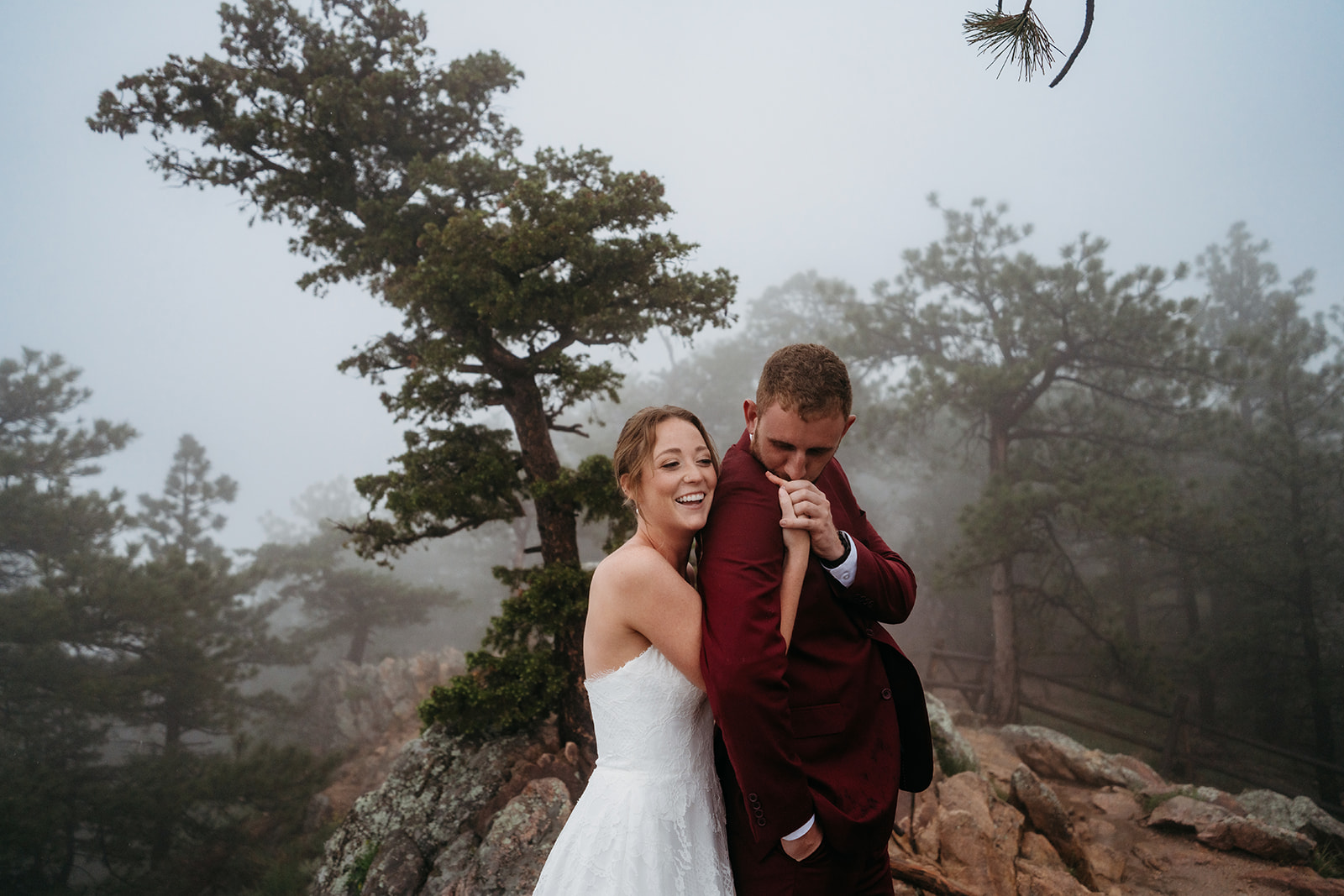 Newlyweds laughing together on a misty mountain ledge, showing the joy of how to plan an elopement.