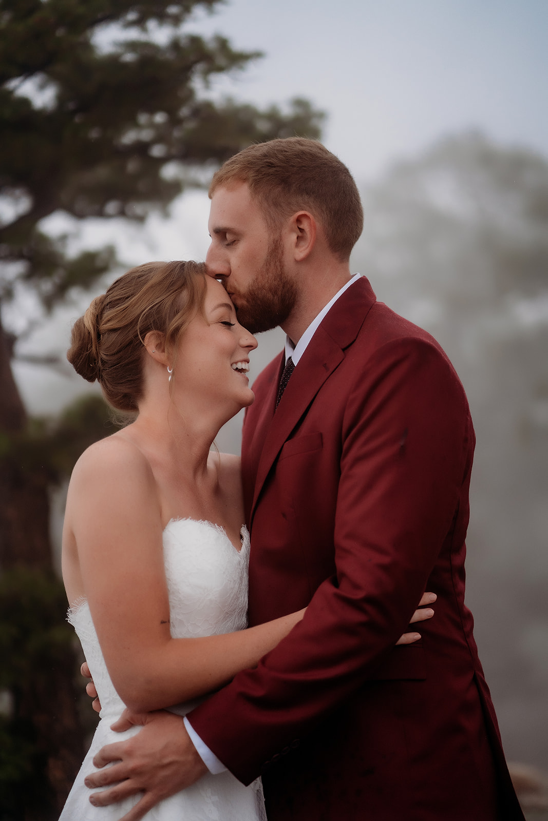 Groom kissing his bride’s forehead while holding her close, an intimate elopement moment.