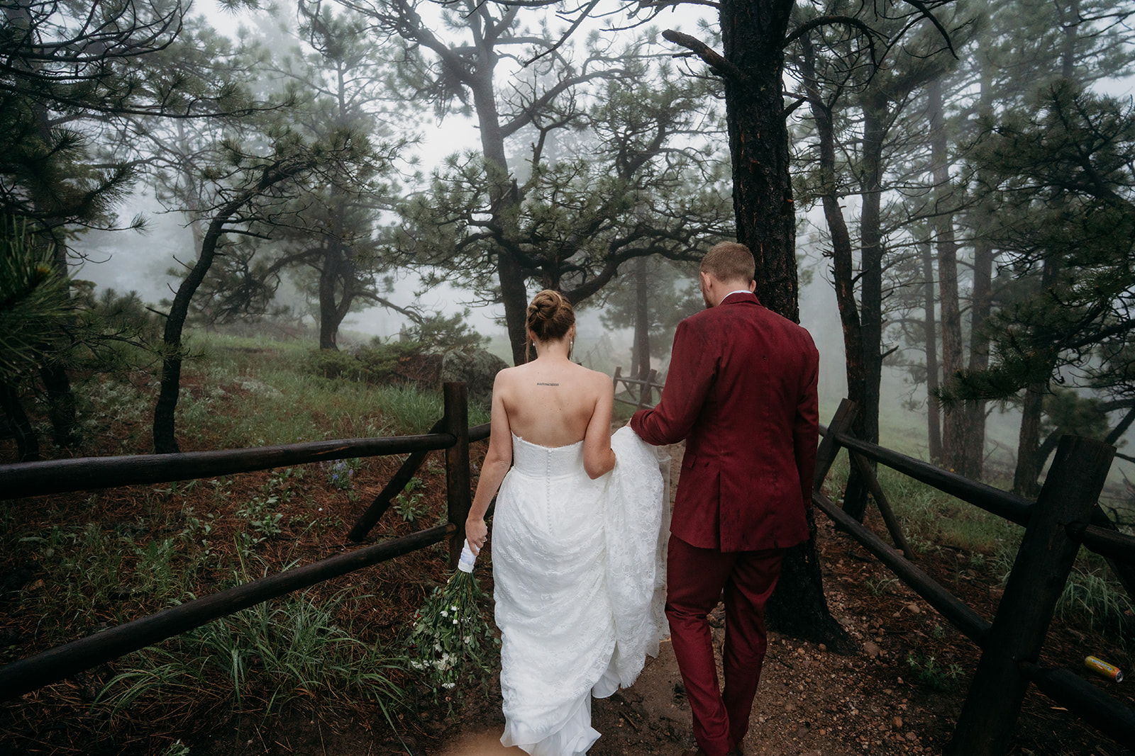 Bride and groom walking side by side through a foggy forest path, holding hands and bouquet.