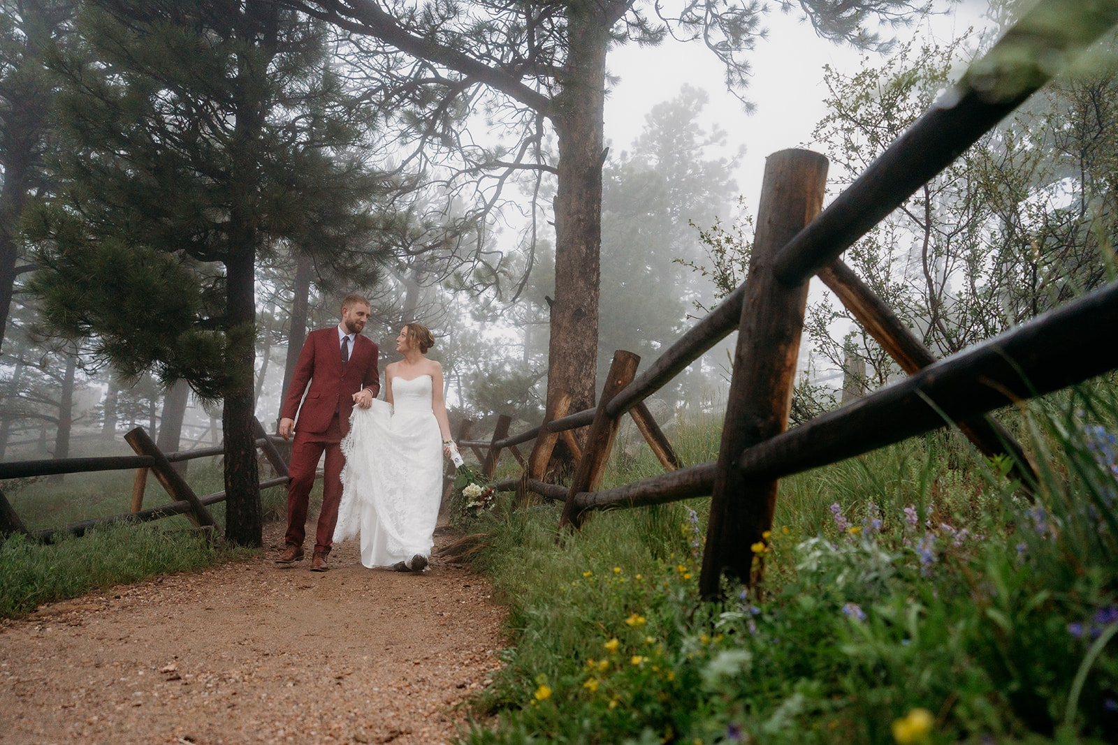 Bride and groom walking hand in hand down a wooded trail lined with wildflowers on their elopement day.