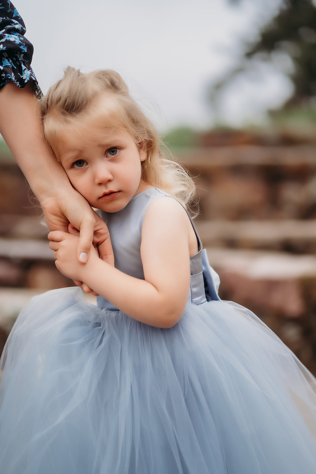 Young flower girl in a blue tulle dress holding tightly to a parent’s hand during the wedding.