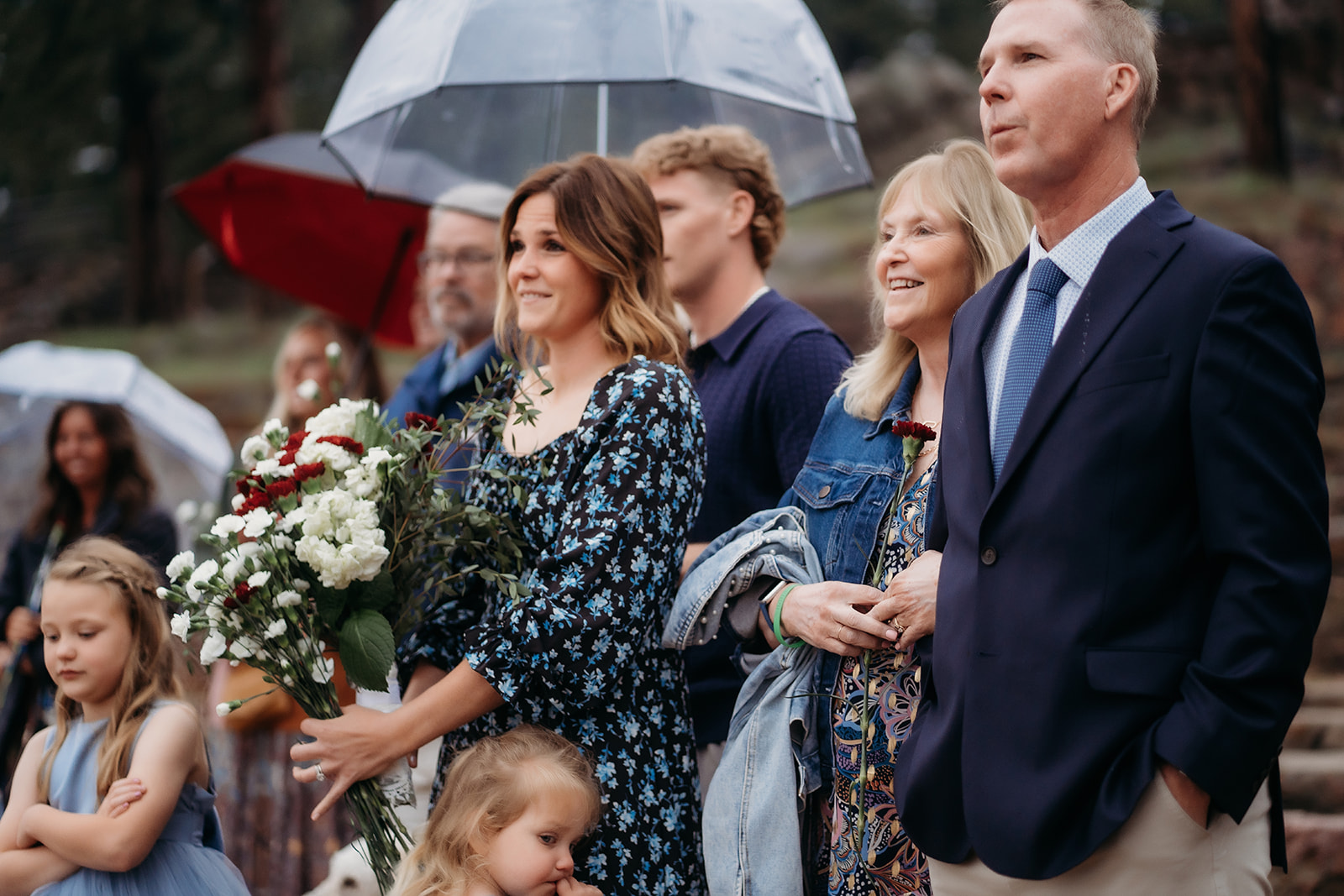 Guests holding flowers and umbrellas watch the couple exchange vows during the ceremony.