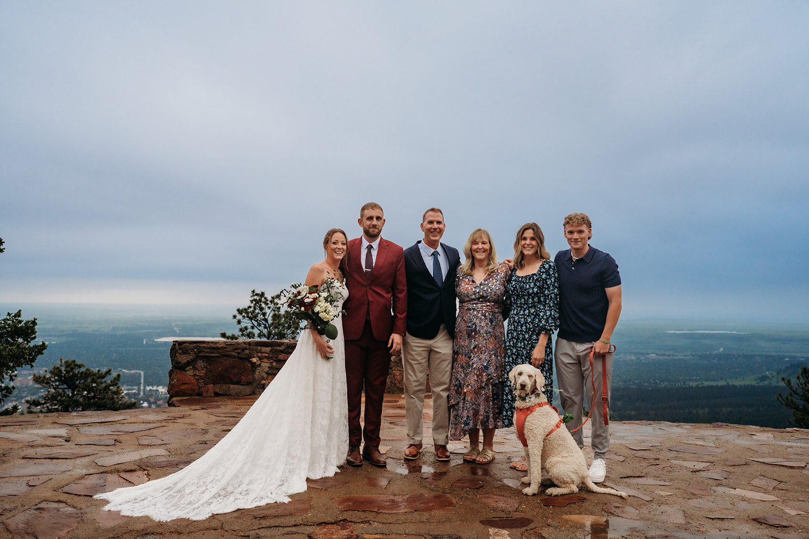 Bride and groom posing with family and their dog on a scenic overlook, celebrating after their elopement.