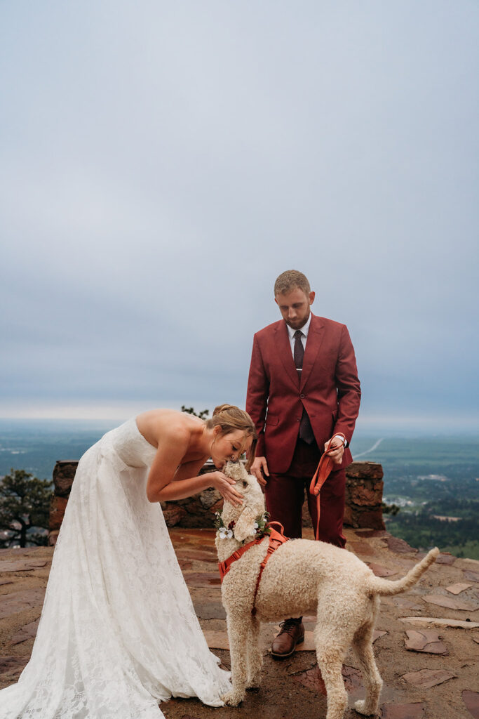 Bride kneels to kiss her dog wearing a floral collar, a personal touch in How to Plan an Elopement.