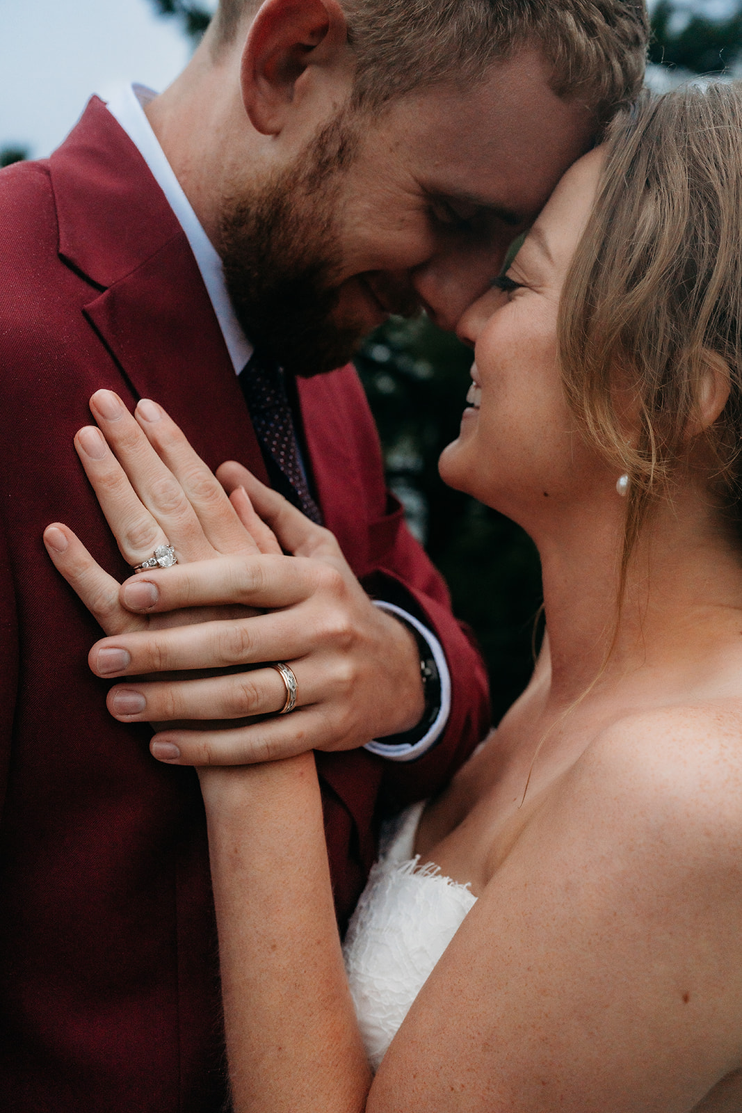 Couple leaning into each other and smiling, showing their rings after their mountain elopement.