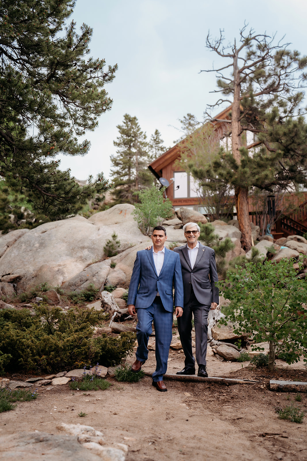 Two groomsmen walking down a rocky mountain path toward a Colorado cabin during an adventure elopement.