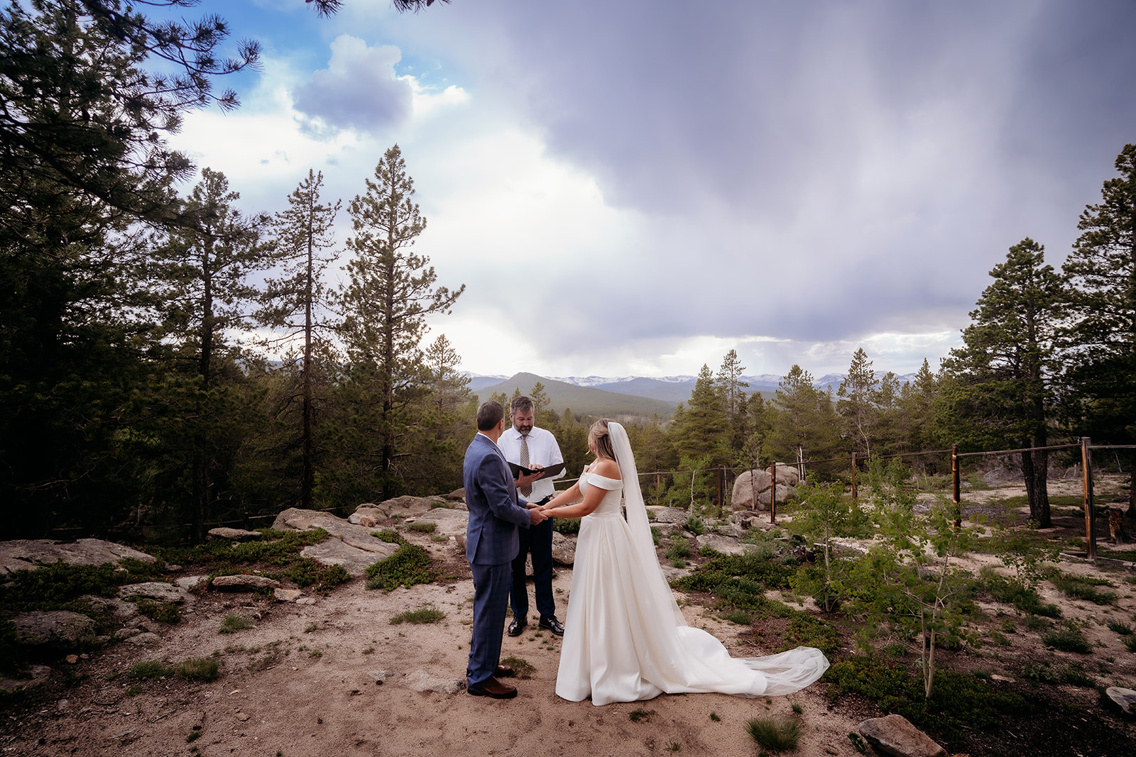 Wide shot of bride and groom with officiant against dramatic skies during their Colorado adventure elopement.