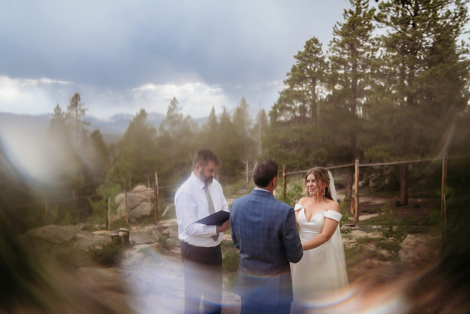 Artistic photo of bride and groom with officiant framed by light flares during their Colorado adventure elopement ceremony.